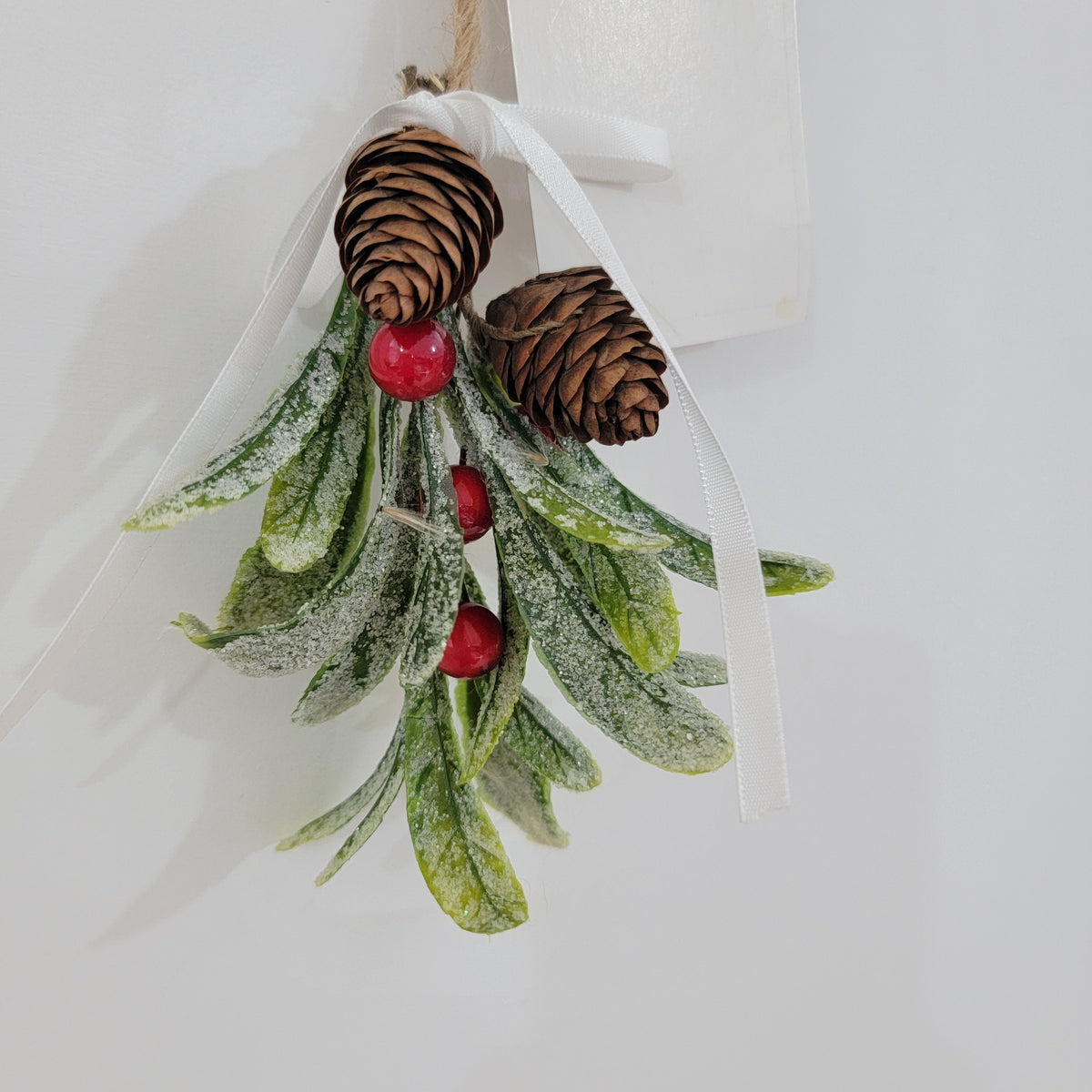 Artificial mistletoe decoration with green leaves and white, gold berries, tied with a ribbon, perfect for holiday decor.